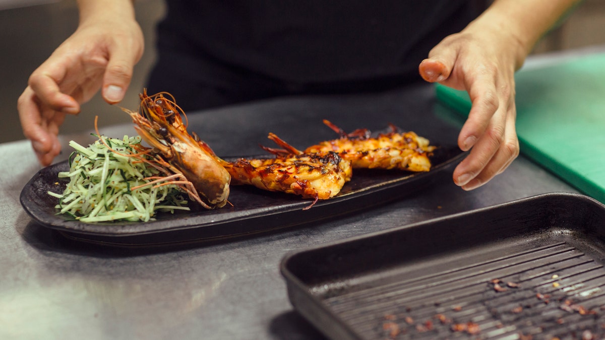 Chef working in his kitchen in restaurant. Shot of his hands preparing asian food. Preparing grilled king prawn. This is real chef not model.