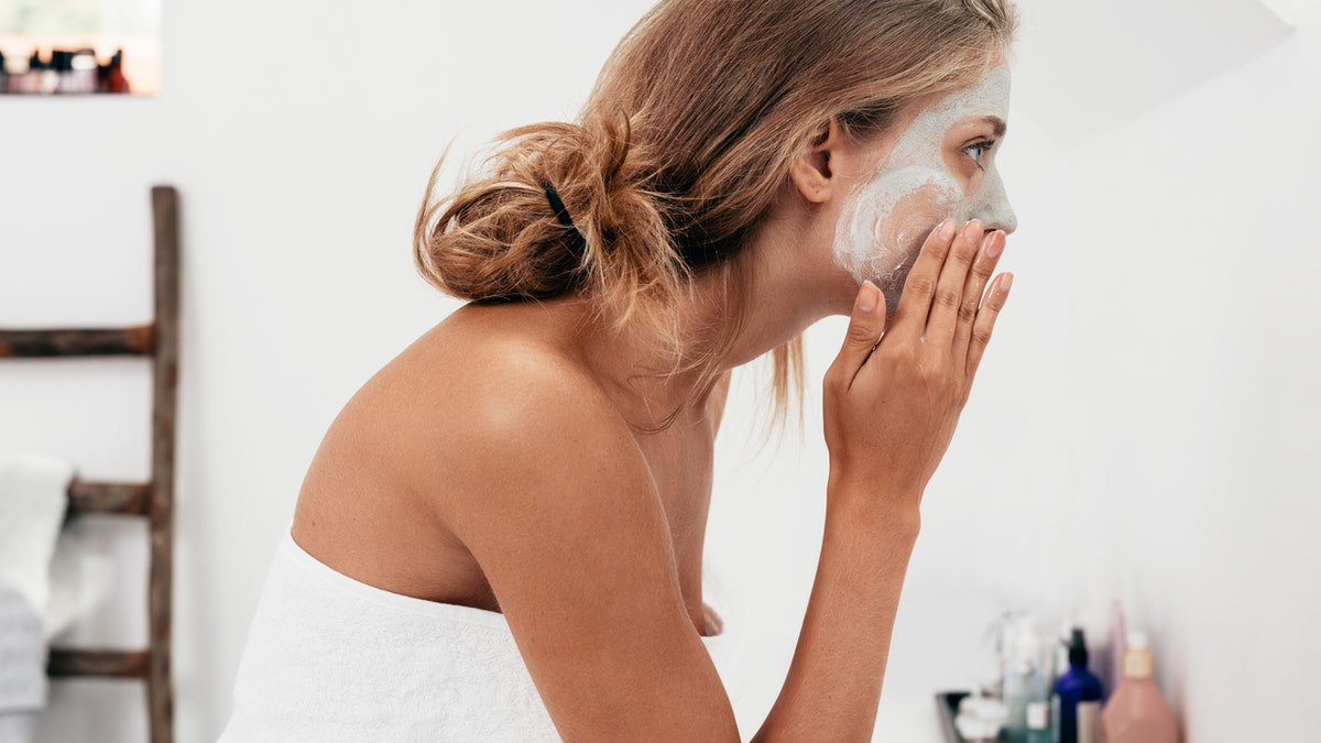 Side view shot of young woman applying facial cosmetic mask in bathroom. Female taking care of her face skin.