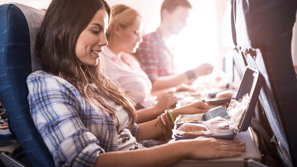 Three passengers traveling by plane and having their meal. Focus is on happy woman in the foreground.
