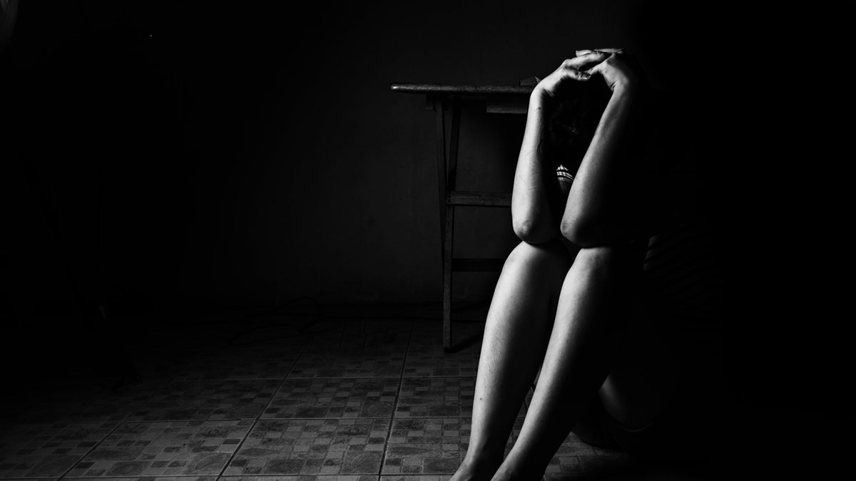 a woman sitting on ground with arm around lower head, sexual violence , sexual abuse, human trafficking concept with shadow edge in white tone