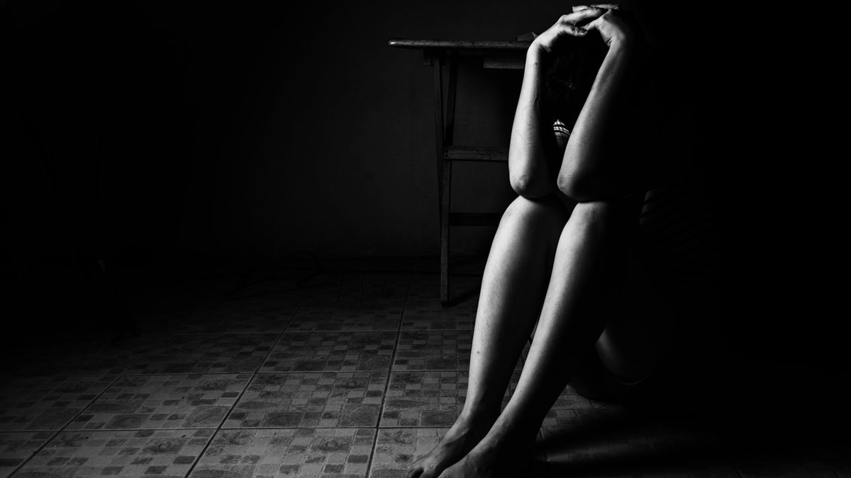 a woman sitting on ground with arm around lower head, sexual violence , sexual abuse, human trafficking concept with shadow edge in white tone