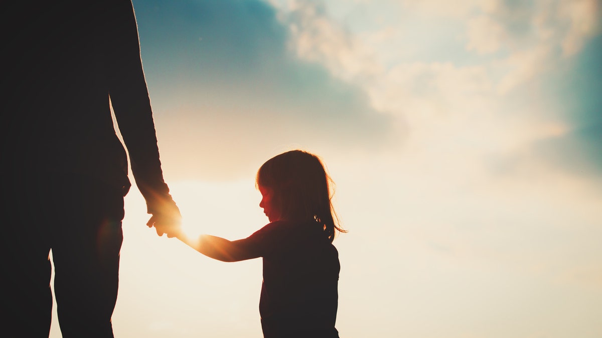 silhouette of little girl holding parent hand at sunset, parenting concept