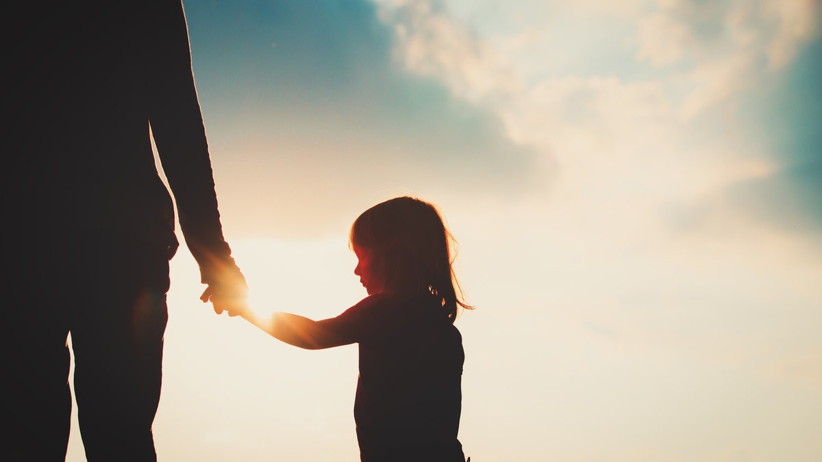 silhouette of little girl holding parent hand at sunset, parenting concept