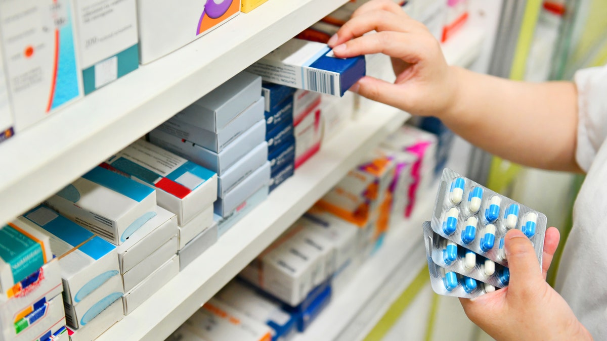 Pharmacist holding medicine box and capsule pack in pharmacy drugstore.