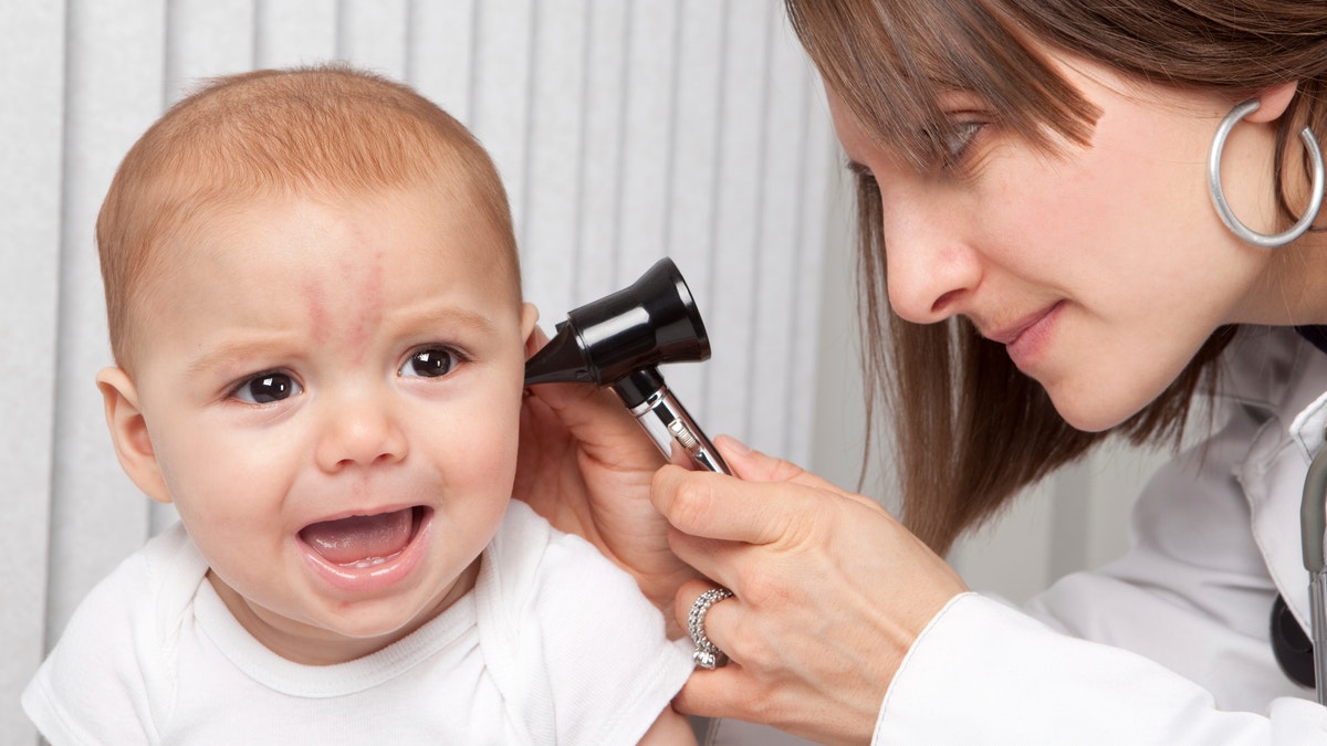 A pediatrician using an otoscope to look into the ear of an 8 month old baby boy.