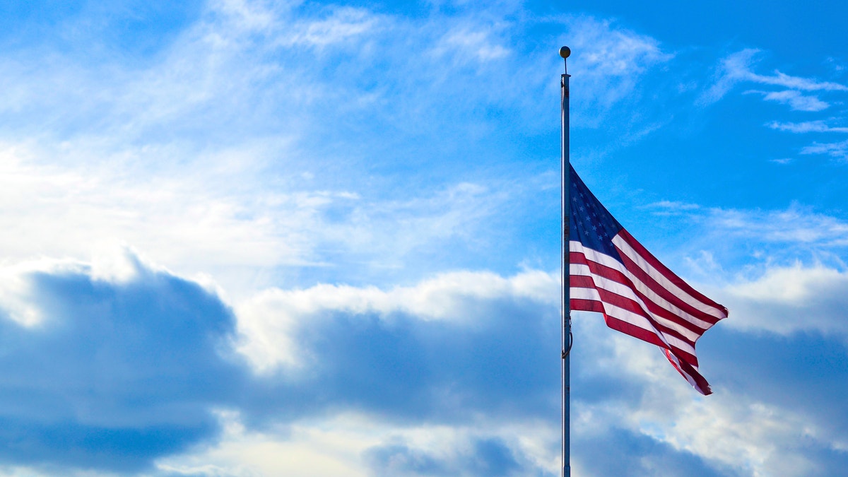 This half-mast American flag was captured against a perfect blue sky full of clouds.