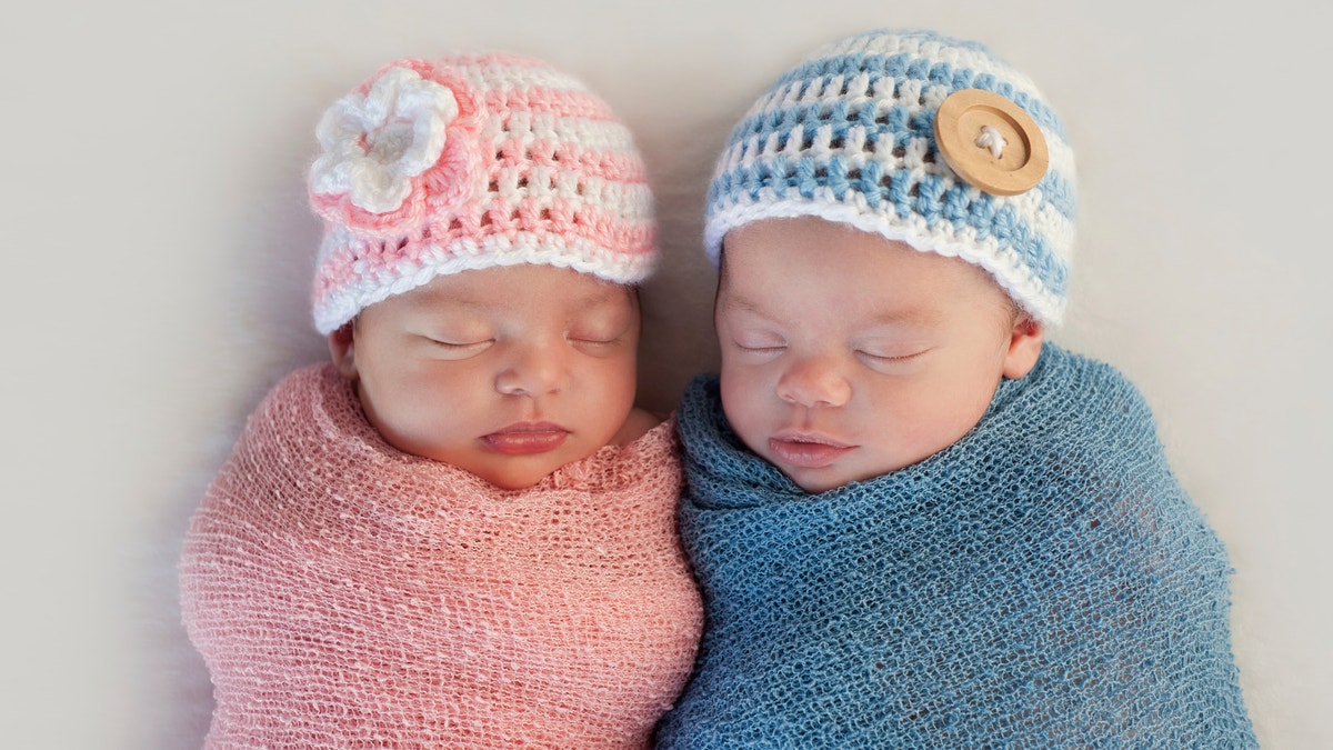 Five week old sleeping boy and girl fraternal twin newborn babies. They are wearing crocheted pink and blue striped hats.