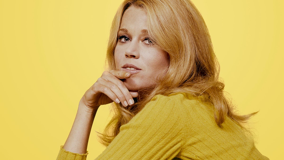 Portrait of American actress Jane Fonda, her hand on her chin, as she poses in a yellow sweater against a yellow background, 1960s.