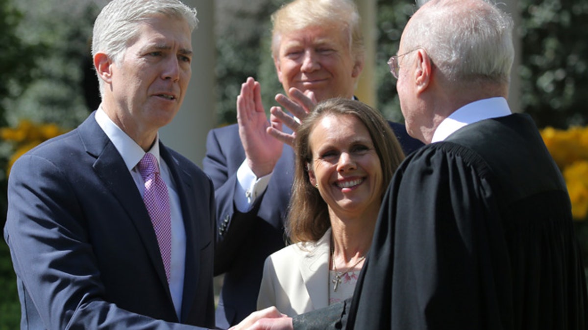 Judge Neil Gorsuch shakes hands with Supreme Court Associate Justice Anthony Kennedy after being sworn in as an Associate Justice of the Supreme Court, accompanied by Louise Gorsuch (C) and U.S. President Donald J. Trump in the Rose Garden of the White House in Washington, U.S., April 10, 2017. REUTERS/Carlos Barria - RTX34YQB