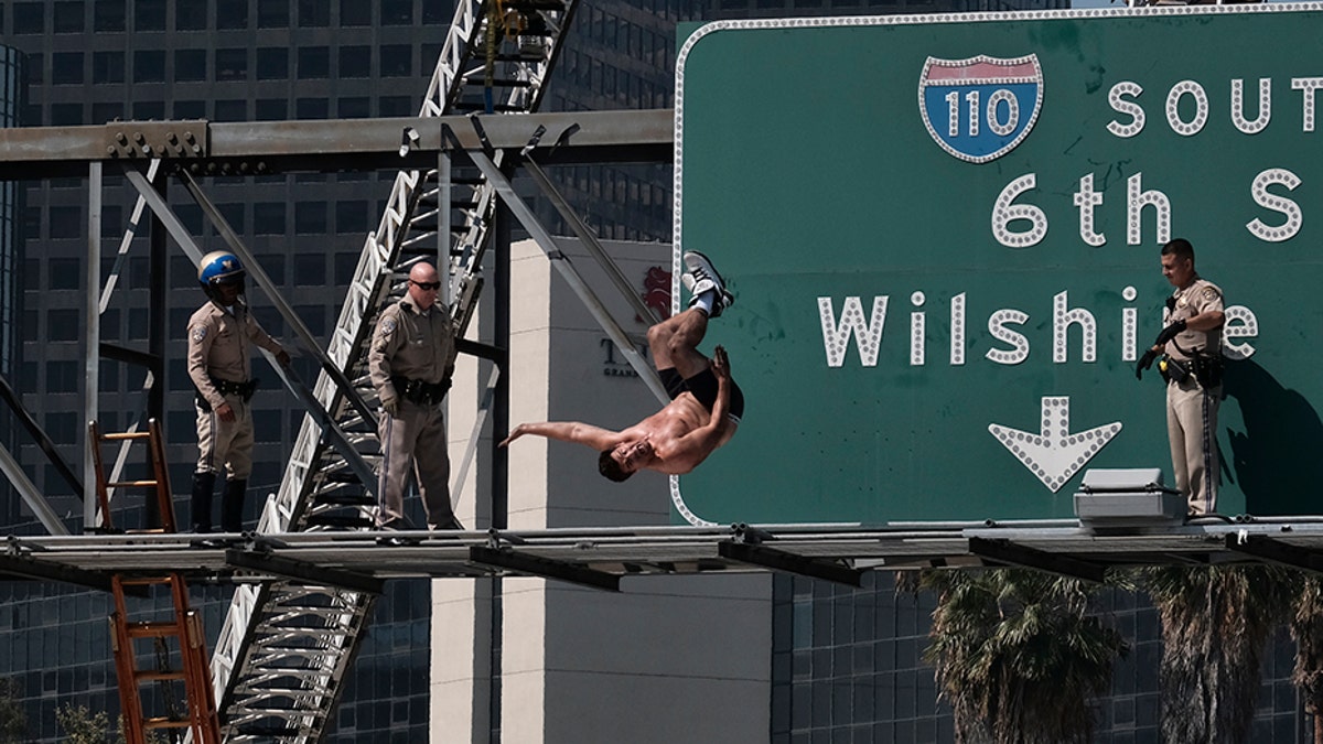 California Highway Patrol officers watch as a man jumps from a highway sign in downtown Los Angeles on Wednesday, June 27, 2018. The man suspended banners, one about fighting pollution, after climbing onto the sign over State Route 110 during the Wednesday morning rush hour. The man did a backflip from the sign and landed on a huge inflated air bag deployed in traffic lanes by firefighters. (AP Photo/Richard Vogel)