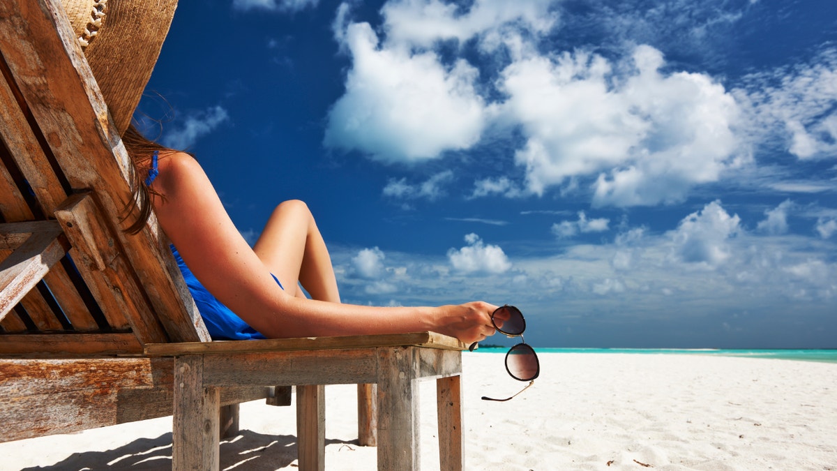 Woman at beach holding sunglasses