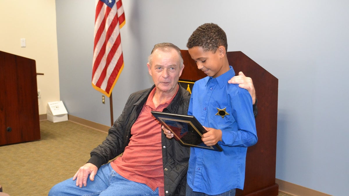 Malachi Coffey inspects his plaque as he stands next to Allen Clemmons. The 65-year-old man was nearly crushed by his Mustang convertible on March 10.