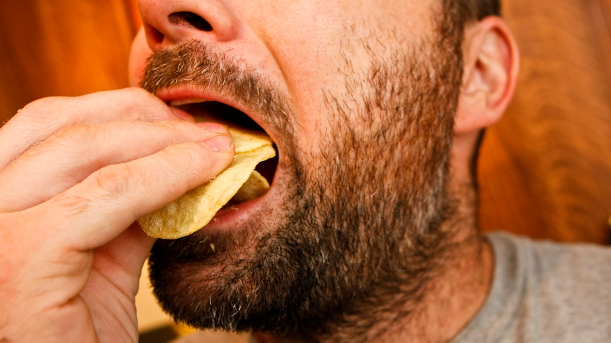 man eating potato chips istock