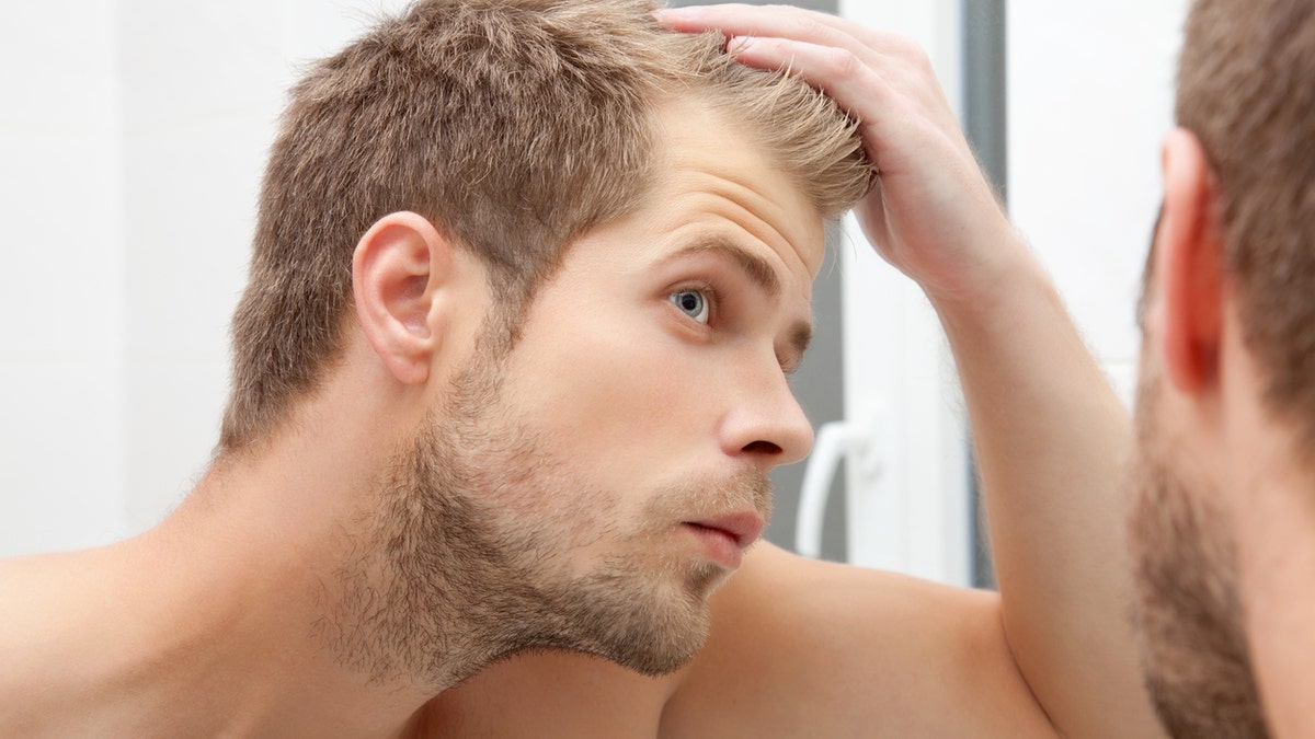 Handsome unshaven man looking into the mirror in bathroom