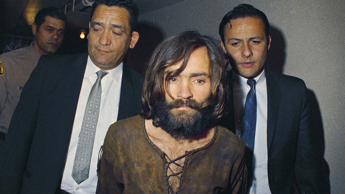 FILE - In this 1969 file photo, Charles Manson is escorted to his arraignment on conspiracy-murder charges in connection with the Sharon Tate murder case. A Los Angeles judge on Friday, Jan. 26, 2018, will hear arguments on what county should decide who gets the remains of cult leader Manson who orchestrated the 1969 killings of pregnant actress Tate and eight others. Three camps with alleged ties to Manson, who died in Nov. 2017, claim they want to properly bury or dispose of Manson's ashes, though they allege others want to profit off the remains. (AP Photo, File)