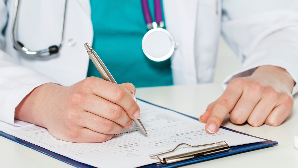 Female medicine doctors hands filling patient medical form. Physician working with paper in hospital office room. Therapeutist sitting at working table making some paperwork. Hands holding silver pen