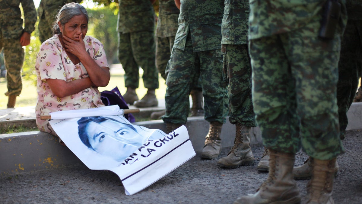 FILE - In this Dec. 18, 2014 file photo, the mother of missing college student Adan Abarajan de la Cruz sits at the foot of soldiers outside a military base during a protest by the families of 43 missing students over the army's alleged responsibility or lack of response to the students' disappearance in Iguala, Mexico. A group of independent experts said Monday, Aug. 17 2015, that Mexican authorities withheld information from family members of 43 college students who disappeared after a confrontation with police, not notifying them that some of the young menâs clothing was discovered shortly after they went missing. (AP Photo/Felix Marquez, File)