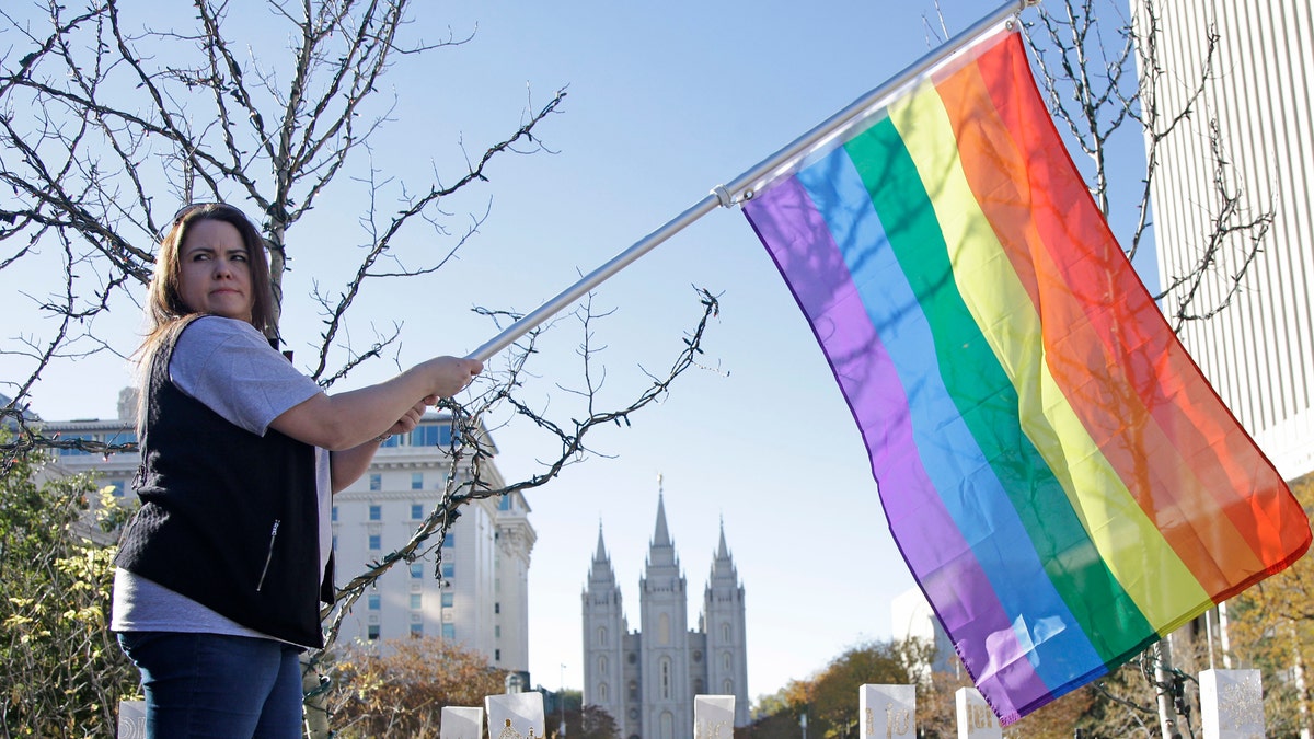 FILE - In this Nov. 14, 2015, file photo, Sandy Newcomb poses for a photograph with a rainbow flag as Mormons gather for a mass resignation from the Church of Jesus Christ of Latter-day Saints, in Salt Lake City. Mormon leaders are telling gay and lesbian church members that attraction to people of the same sex is not a sin or a measure of their faithfulness. But they are reminding those members that acting on those feelings by having sex violates fundamental doctrinal beliefs that won't change. The message is part of the Mormon church's "Mormon and Gay" website launched Tuesday, Oct. 25, 2016, with dozens of articles, teachings, videos and stories from Mormons who identify themselves as gay. (AP Photo/Rick Bowmer, File)