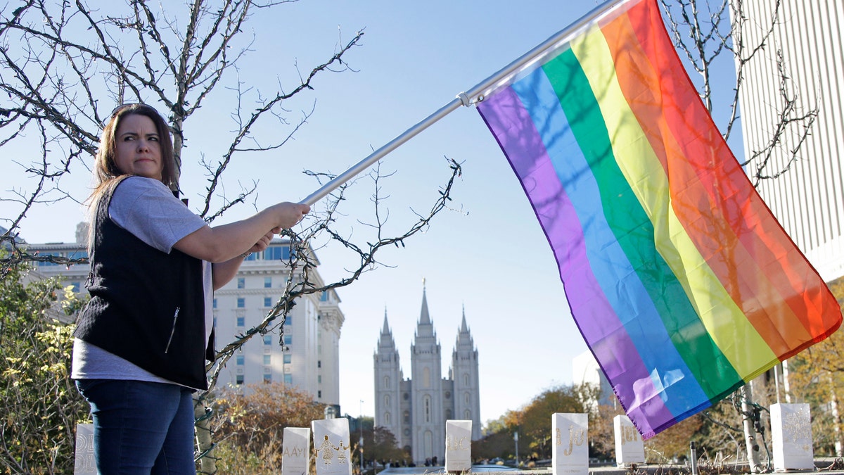 FILE - In this Nov. 14, 2015, file photo, Sandy Newcomb poses for a photograph with a rainbow flag as Mormons gather for a mass resignation from the Church of Jesus Christ of Latter-day Saints, in Salt Lake City. Mormon leaders are telling gay and lesbian church members that attraction to people of the same sex is not a sin or a measure of their faithfulness. But they are reminding those members that acting on those feelings by having sex violates fundamental doctrinal beliefs that won't change. The message is part of the Mormon church's "Mormon and Gay" website launched Tuesday, Oct. 25, 2016, with dozens of articles, teachings, videos and stories from Mormons who identify themselves as gay. (AP Photo/Rick Bowmer, File)