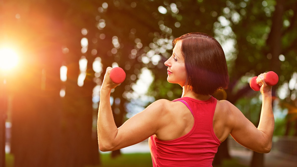 Aged woman working out with small dumbbells in the park in the morning.