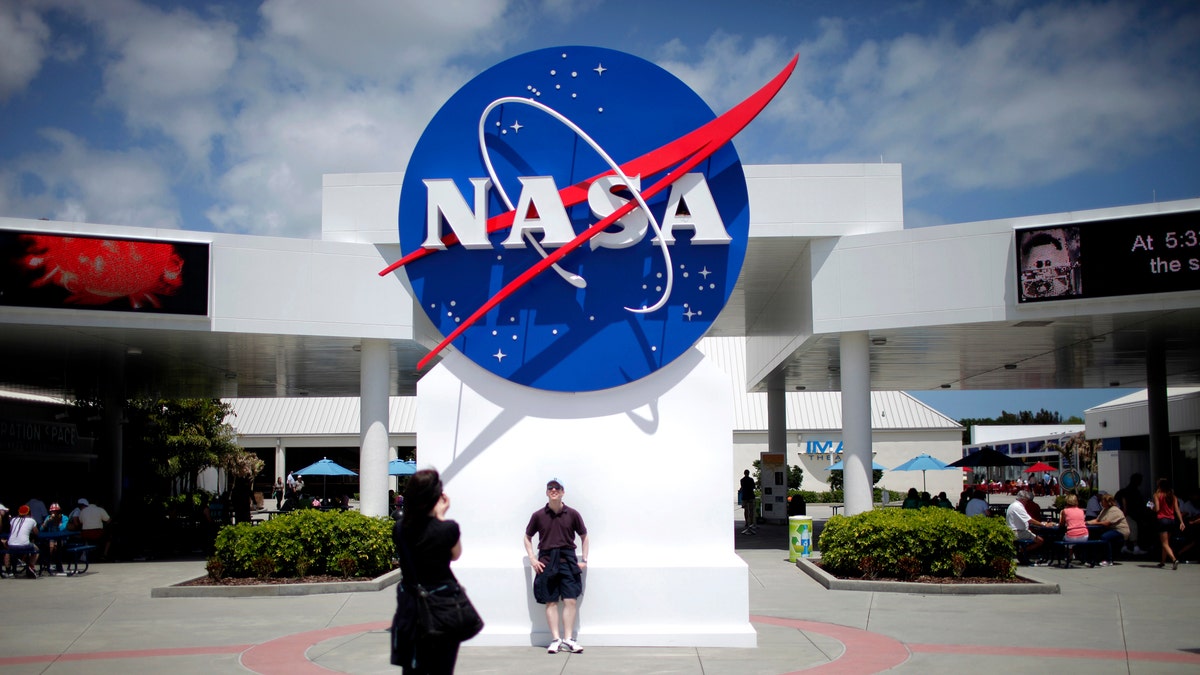 Tourists take pictures of a NASA sign at the Kennedy Space Center visitors complex in Cape Canaveral, Florida April 14, 2010. President Barack Obama will outline a revamped space policy on Thursday aimed at speeding development of a new heavy-lift rocket, increasing the number of human spaceflight missions, creating 2,500 new jobs and ultimately voyaging to Mars.  REUTERS/Carlos Barria (UNITED STATES - Tags: POLITICS SCI TECH) - RTR2CTIK