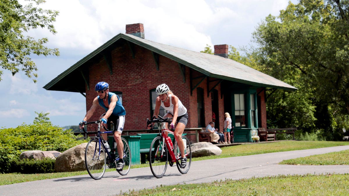 FILE- In this Tuesday, Aug. 4, 2015 file photo, cyclists pass the Niskayuna Train Station as they bike on the Canalway Trail in Niskayuna, N.Y. Gov. Andrew Cuomo proposed a a 750-mile paved biking and hiking Empire State Trail, of which the Canalway Trail would be part of. (AP Photo/Mike Groll, File)