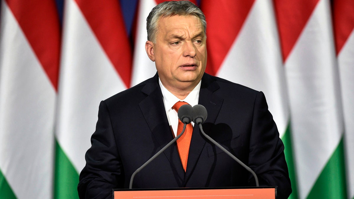 Orban with Hungarian flags behind him at podium