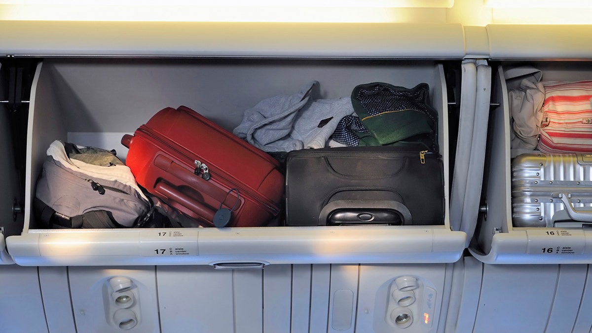 Carry-on luggage in overhead storage compartment on commercial airplane.