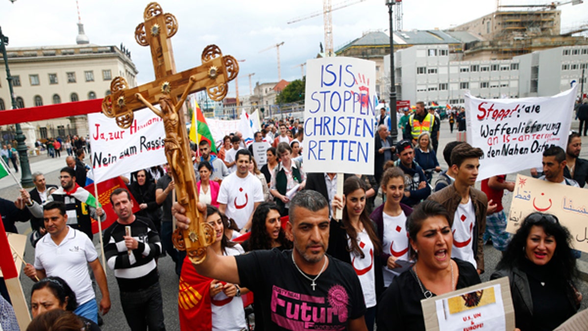 People holds crosses and signs during a rally organised by Iraqi Christians living in Germany denouncing what they say is repression by the Islamic State militant group against Christians living in Iraq, in Berlin, August 17, 2014. Some of the signs read 