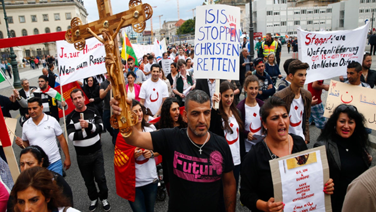 People holds crosses and signs during a rally organised by Iraqi Christians living in Germany denouncing what they say is repression by the Islamic State militant group against Christians living in Iraq, in Berlin, August 17, 2014. Some of the signs read 