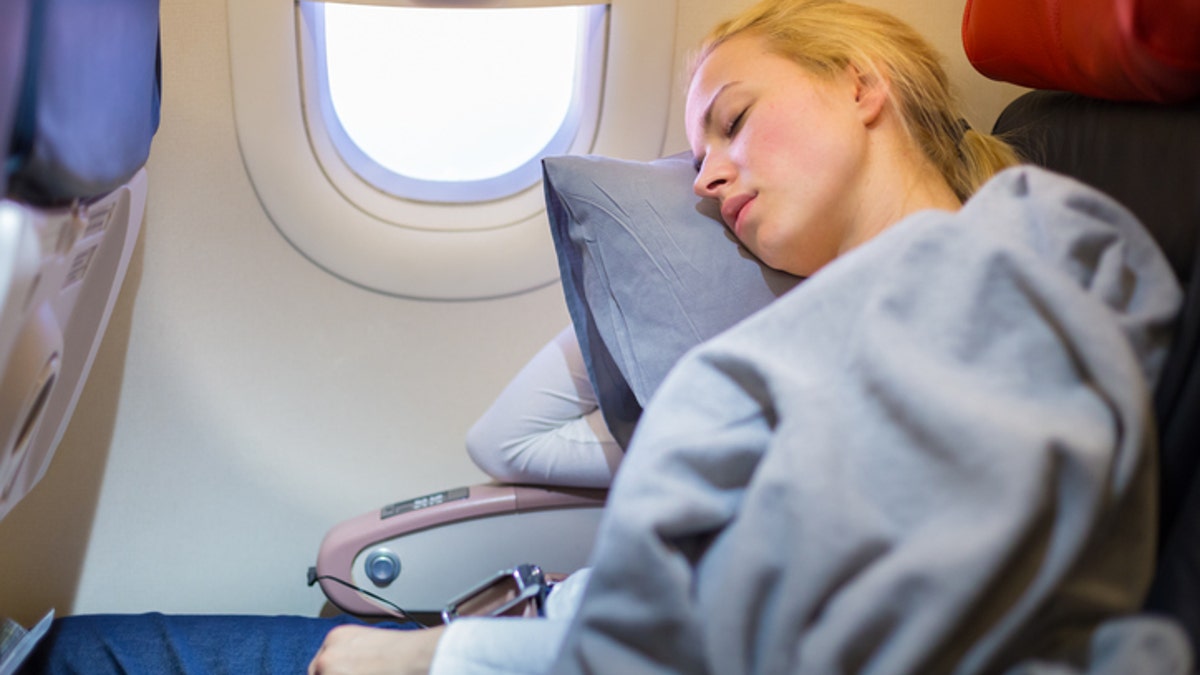 Tired blonde casual caucasian lady napping on uncomfortable seat while traveling by airplane. Commercial transportation by planes.