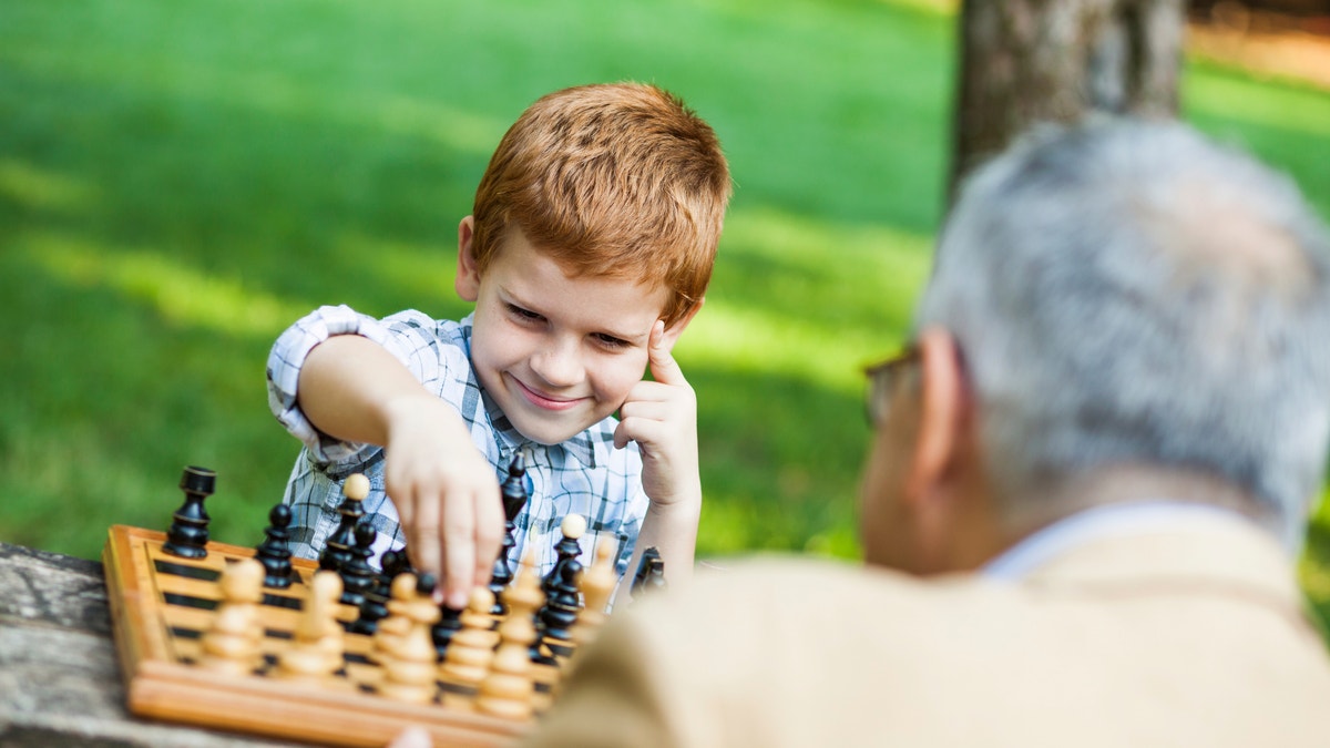 Grandfather and grandson playing a game of chess in park