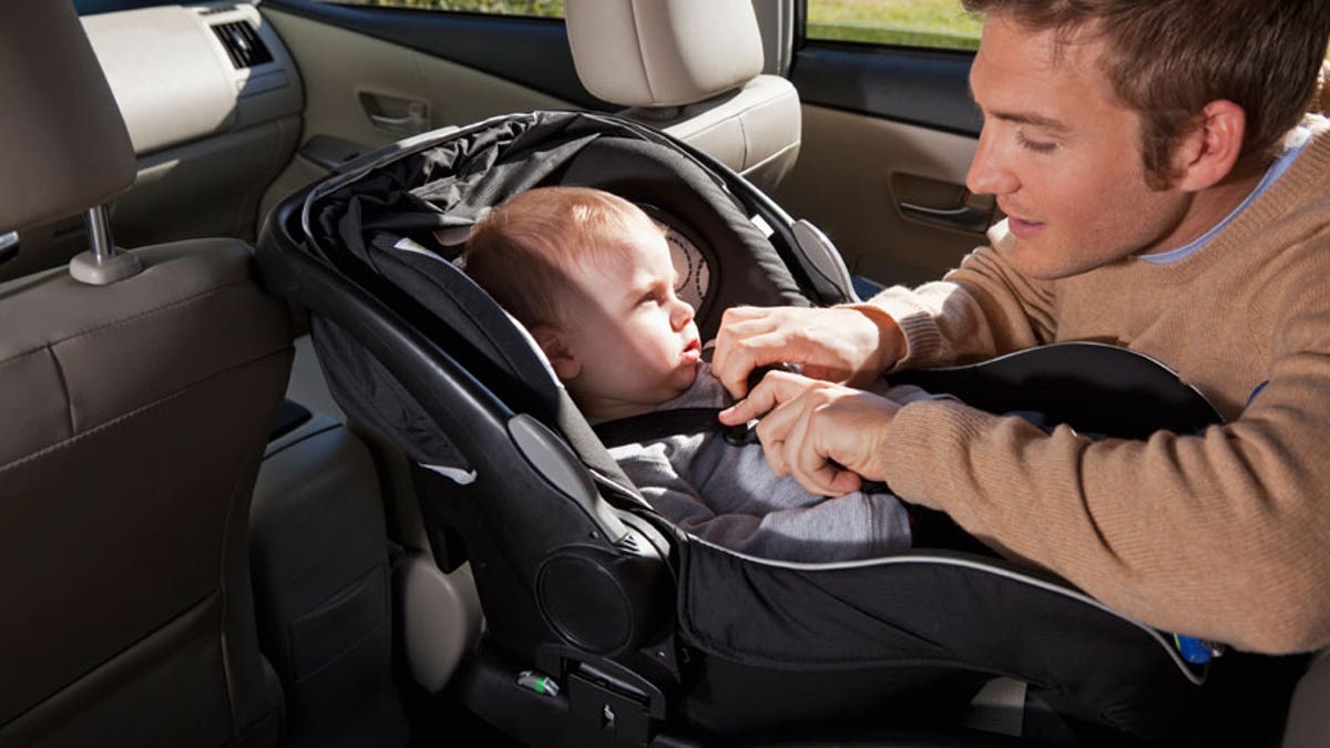 Father buckling baby into car seat