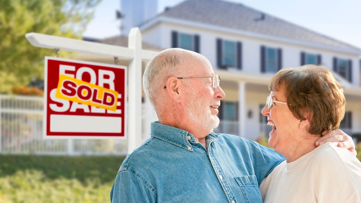 Senior Couple in Front of Sold Real Estate Sign, House