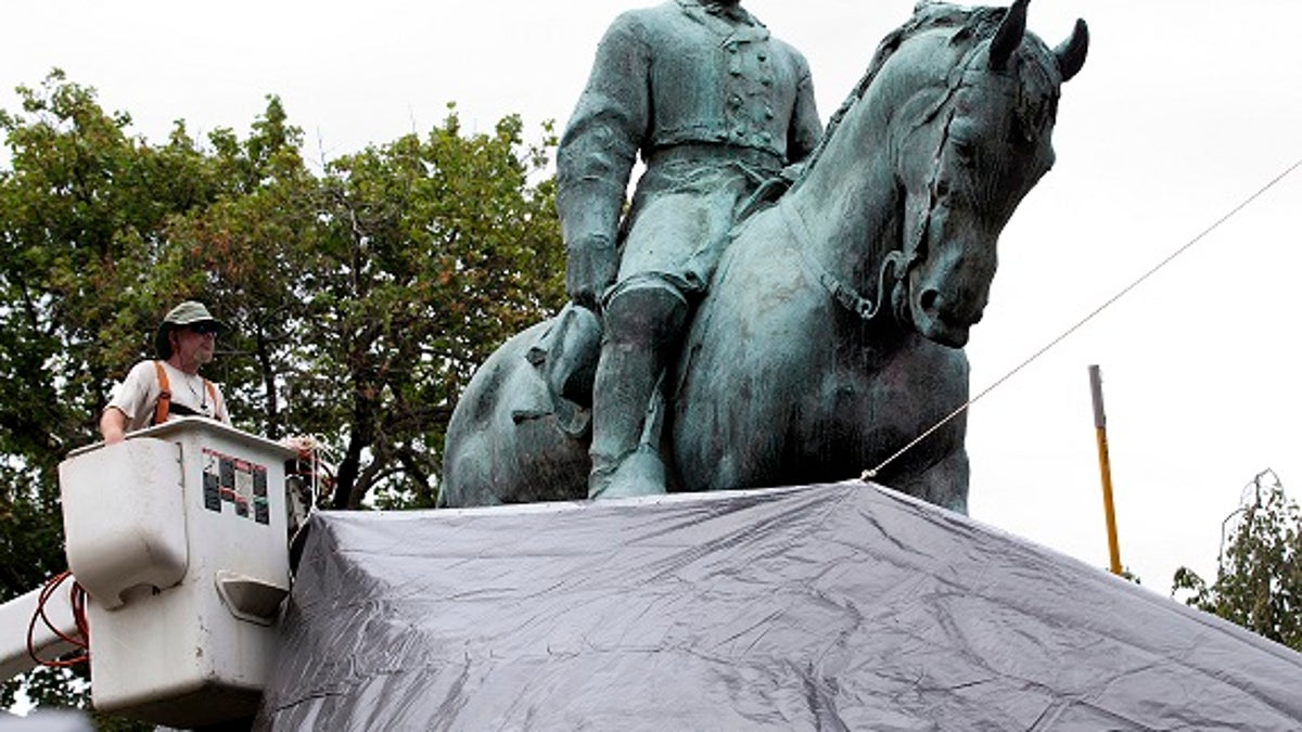 City workers drape a tarp over the statue of Confederate General Robert E. Lee in Emancipation park in Charlottesville, Va., Wednesday, Aug. 23, 2017. The move intended to symbolize the city's mourning for Heather Heyer, killed while protesting a white nationalist rally earlier this month.  (AP Photo/Steve Helber)