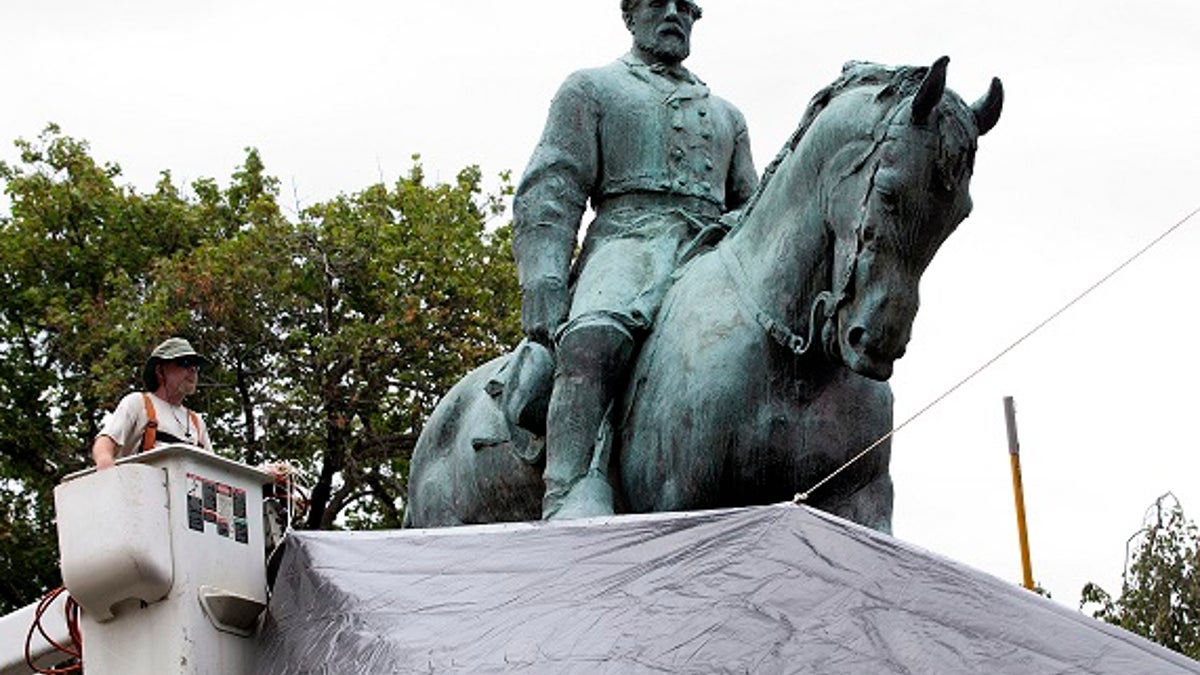 City workers drape a tarp over the statue of Confederate General Robert E. Lee in Emancipation park in Charlottesville, Va., Wednesday, Aug. 23, 2017. The move intended to symbolize the city's mourning for Heather Heyer, killed while protesting a white nationalist rally earlier this month.  (AP Photo/Steve Helber)