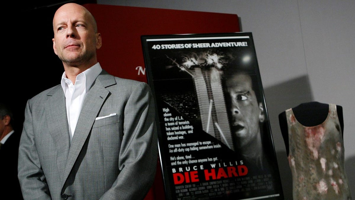 Actor Bruce Willis poses beside a movie poster and shirt from the movie "Die Hard" which he donated to the Smithsonian's National Museum of American History in Washington, June 27, 2007. REUTERS/Jim Young (UNITED STATES) - GM1DVOSGBLAA