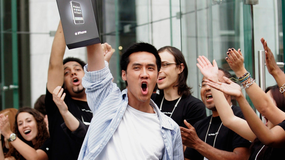 Surrounded by cheering Apple Store employees, one of the first iPhone buyers leaves the store on Fifth Avenue in New York, June 29, 2007. REUTERS/Jeff Zelevansky (UNITED STATES) BEST QUALITY AVAILABLE - RTR1RAZ0