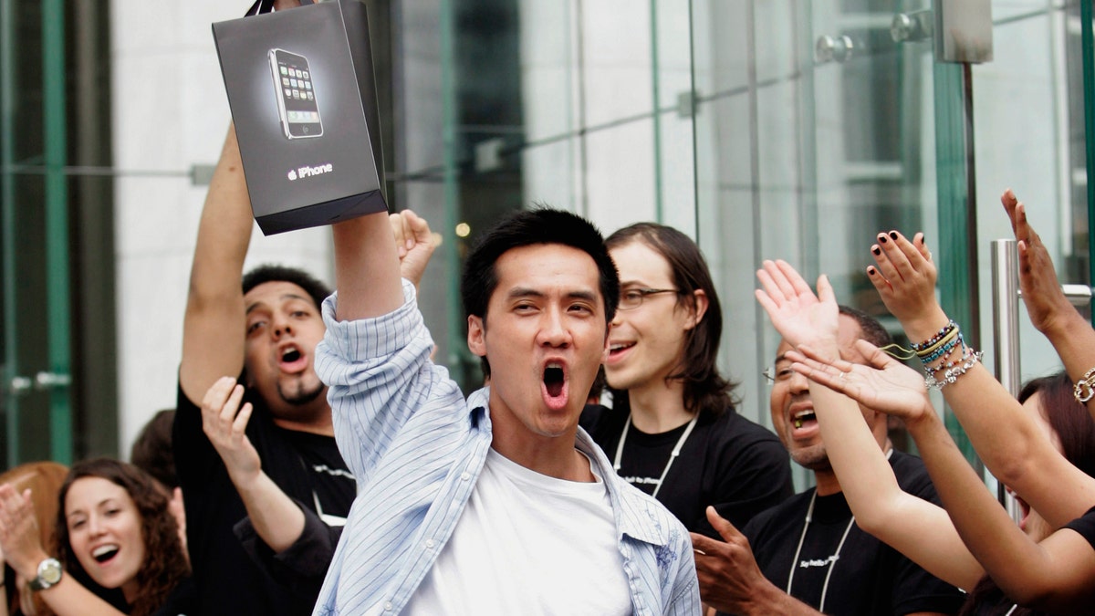 Surrounded by cheering Apple Store employees, one of the first iPhone buyers leaves the store on Fifth Avenue in New York, June 29, 2007. REUTERS/Jeff Zelevansky (UNITED STATES) BEST QUALITY AVAILABLE - RTR1RAZ0