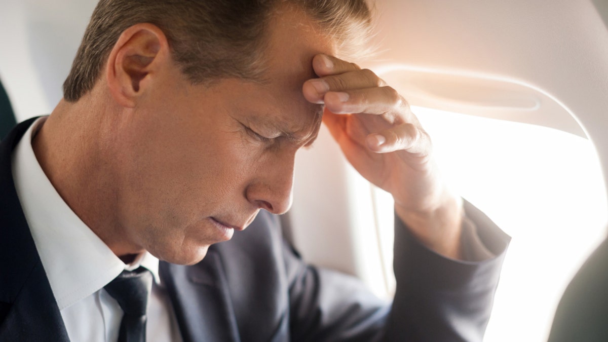 Feeling headache. Frustrated mature businessman touching his forehead with hand and keeping eyes closed while sitting at his seat in airplane 