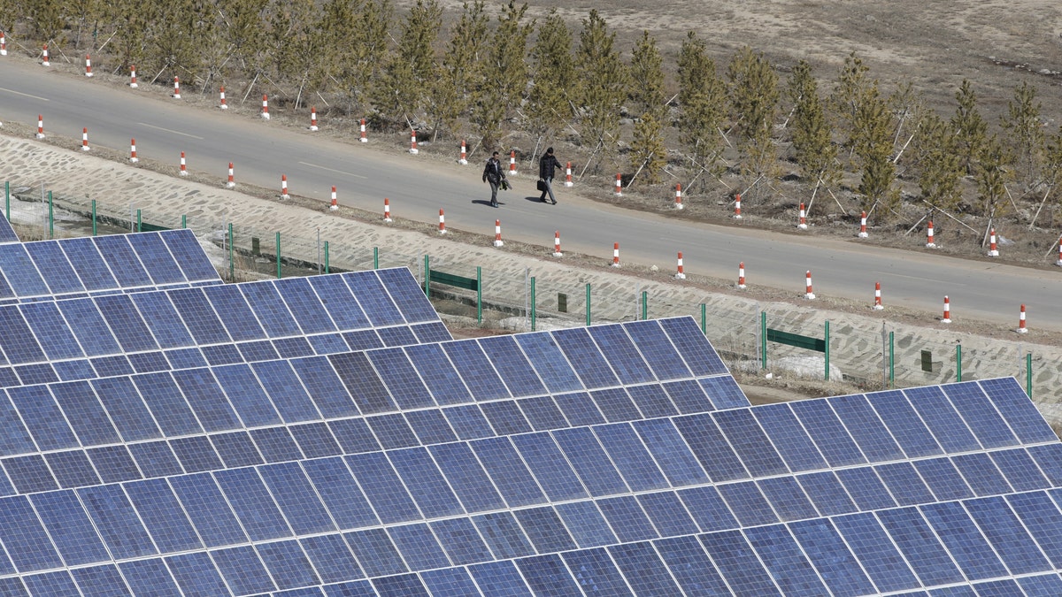 People walk past the solar panels at a wind and solar energy storage and transmission power station of State Grid Corporation of China, in Zhangjiakou of Hebei province, China, March 18, 2016. REUTERS/Jason Lee - RTSB3AZ