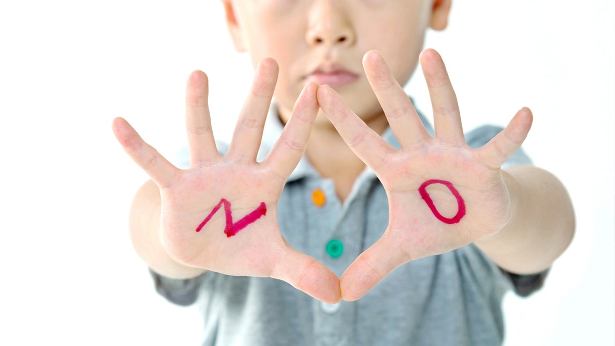 child with hands out and the word 'no' on his hands