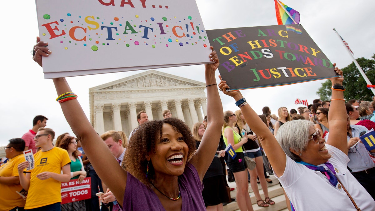 Ikeita Cantu, left, and her wife Carmen Guzman, of McLean, Va., hold up signs as they celebrate outside of the Supreme Court in Washington, Friday June 26, 2015, after the court declared that same-sex couples have a right to marry anywhere in the US. The couple was married in Canada in 2009 when gay marriage was illegal in Virginia. (AP Photo/Jacquelyn Martin)