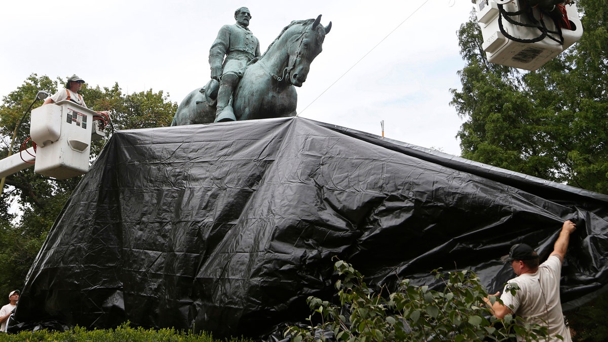 FILE-In this Wednesday, Aug. 23, 2017, file photo, city workers drape a tarp over the statue of Confederate General Robert E. Lee in Emancipation park in Charlottesville, Va. Officials in Charlottesville are trying to stop people from ripping down tarps that cover statues of Confederate generals. (AP Photo/Steve Helber, File)