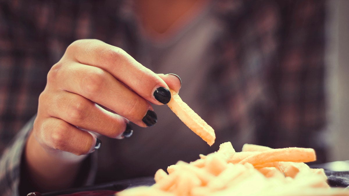 woman hand with green nails toasting french fries in restaurant