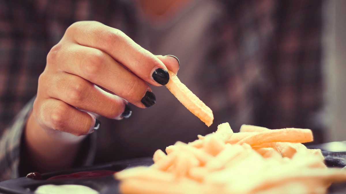 woman hand with green nails toasting french fries in restaurant