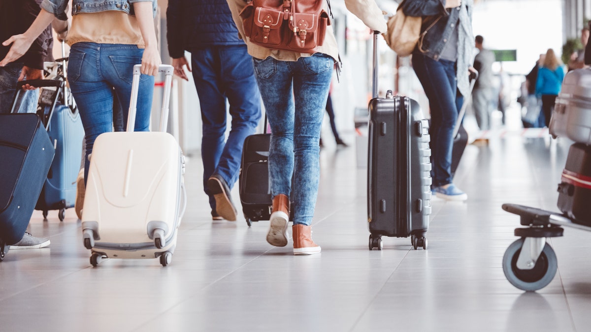 Low angle rear view of passengers walking in the airport terminal. People with luggage in airport.