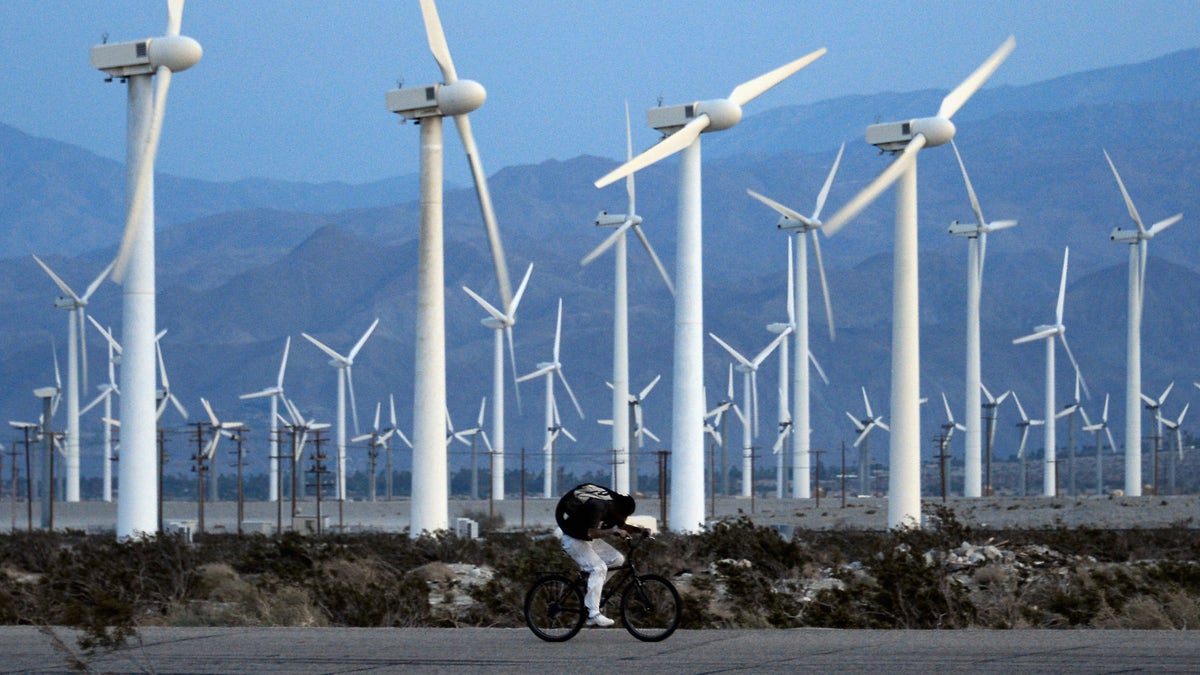 PALM SPRINGS, CA - MARCH 27: A man rids his bike against the win as giant wind turbines are powered by strong winds at sunset on March 27, 2013 in Palm Springs, California. According to reports, California continues to lead the nation in green technology and has the lowest greenhouse gas emissions per capita, even with a growing economy and population. (Photo by Kevork Djansezian/Getty Images)