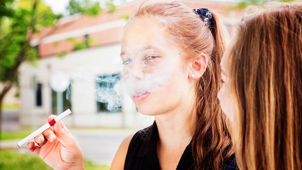 Preteen girl tries e-cigarette under the influence of her friend.