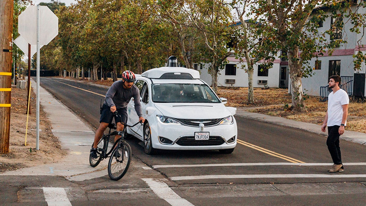 This Sunday, Oct. 29, 2017, photo provided by Waymo shows a Chrysler Pacifica minivan equipped with Waymo's self-driving car technology, being tested with the company's employees as a biker and a pedestrian at Waymo's facility in Atwater, Calif. Waymo, hatched from a Google project started eight years ago, showed off its progress Monday during a rare peek at a closely guarded testing facility located 120 miles southeast of San Francisco where its robots complete their equivalent to driver's education. (Julia Wang/Waymo via AP)